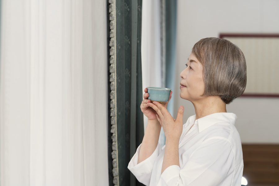 窓辺で湯のみのお茶を飲む女性