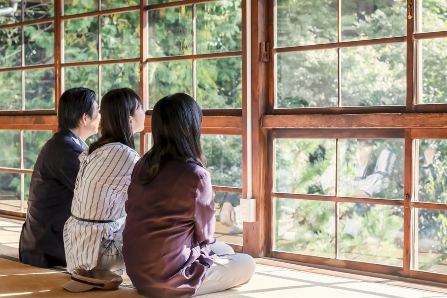 縁側の窓辺に並んで座り、庭を眺める三人の後ろ姿